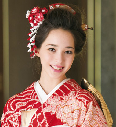 点击大图看下一张：日本女人和服发型图片七：这款发型相当传统，两侧和头顶区都是发髻，搭配一串红色的花朵发饰与和服相得益彰，充分展现日本传统婚礼造型的魅力。