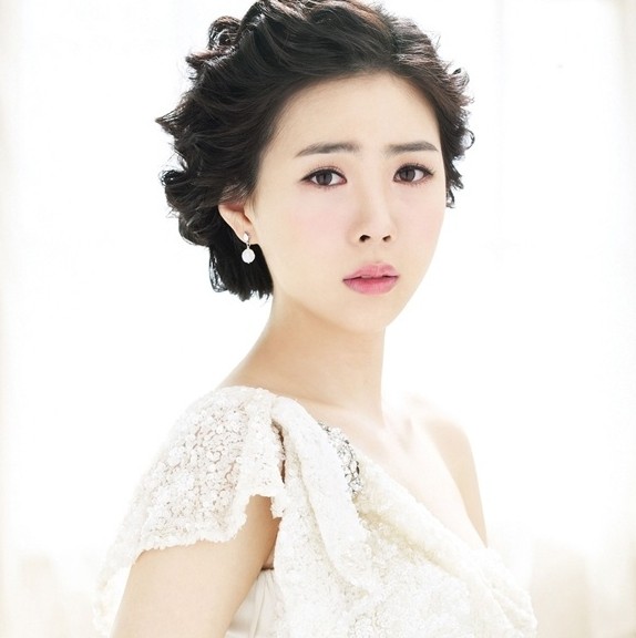 点击大图看下一张：气质优雅韩式新娘盘发发型：发髻与婚纱的完美搭配，如果你是个个性开朗、乐观奔放的新娘，那么这款俏丽的卷曲盘发对你就再合适不过了，还很显气质优雅哦！