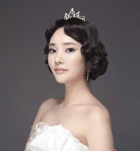 点击大图看下一张：复古风的一款韩式新娘盘发发型，刘海烫卷出的弧度，给人一种高贵典雅的气质，加以皇冠头饰点缀，甜美优雅。