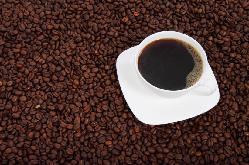 点击大图看下一张：咖啡豆散落在装有咖啡的杯子旁图片
