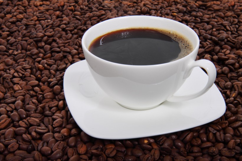 点击大图看下一张：咖啡豆散落在装有咖啡的杯子旁图片