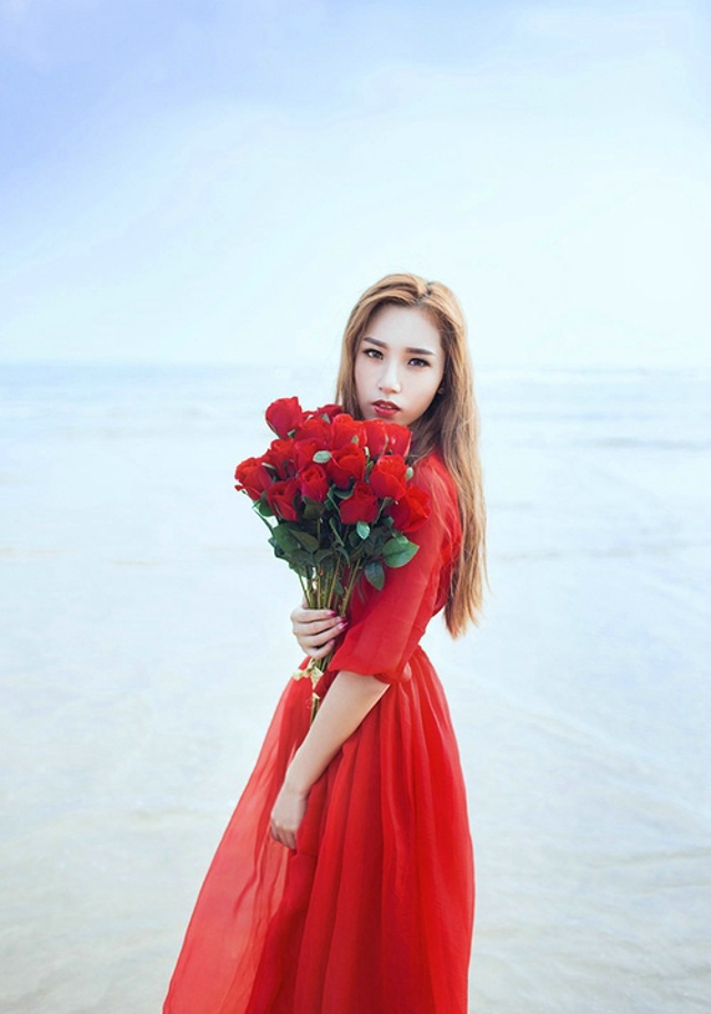 点击大图看下一张：鲜艳红裙美模海边被风吹长发飘逸手捧花令人怜爱