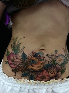遮盖着旧疤痕的喜鹊和花朵腹部纹身